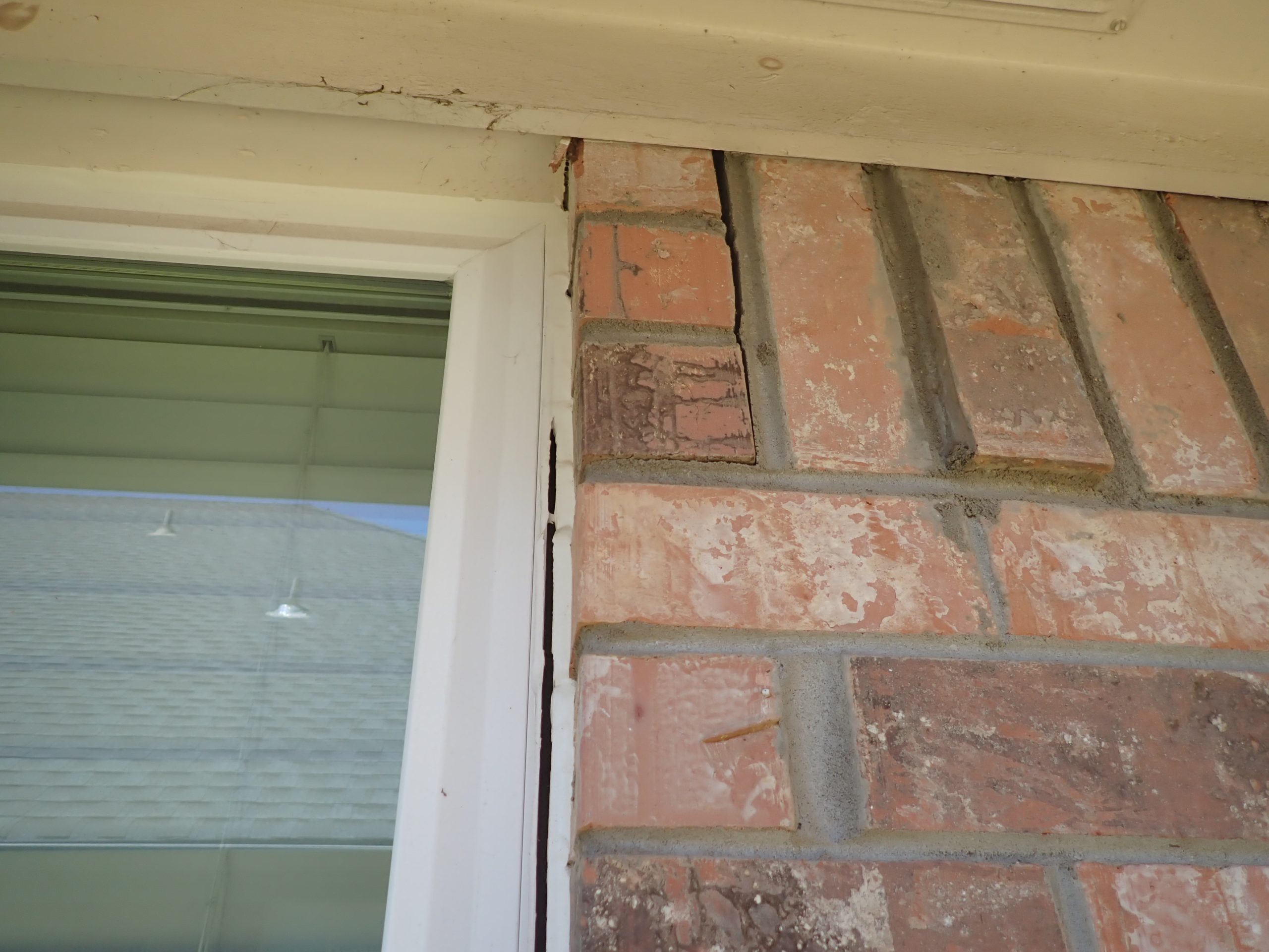 Vertical crack running through brick veneer and mortar joints below a window sill on a North Texas home, consistent with structural movement